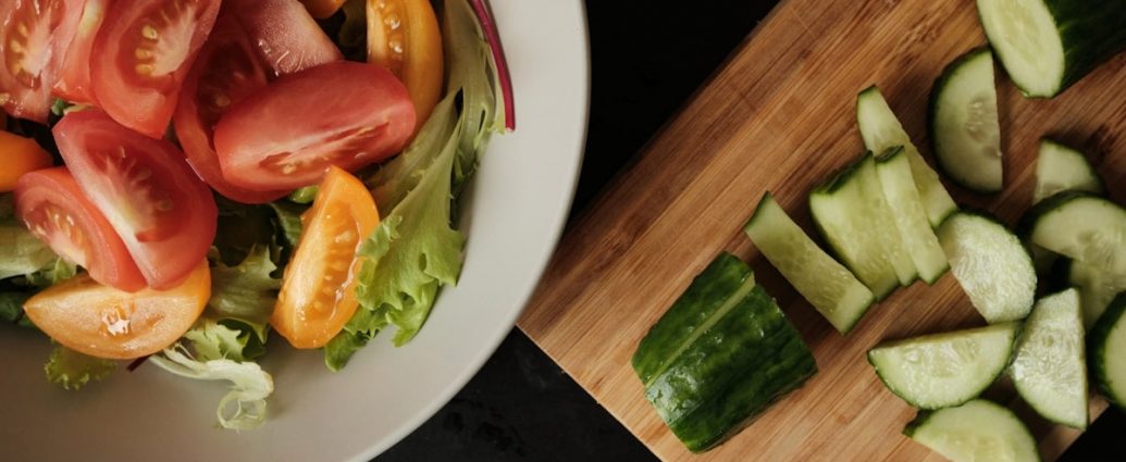 Fresh green salad with cherry tomatoes and sliced cucumber on wooden kitchen board