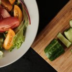 Fresh green salad with cherry tomatoes and sliced cucumber on wooden kitchen board